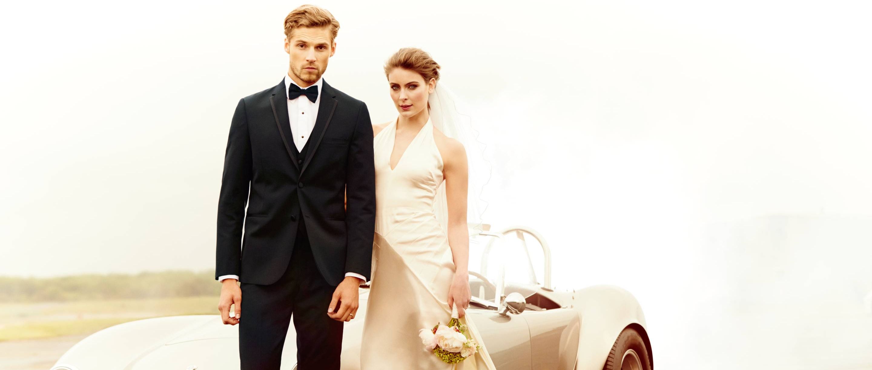 Elegant couple in formal wear standing beside a vintage car